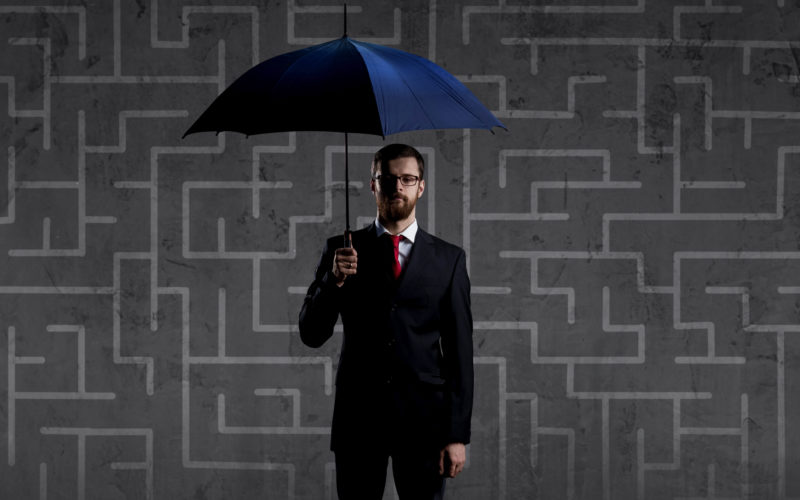 Businessman with umbrella standing over labyrinth background. Business, strategy, insurance, concept.